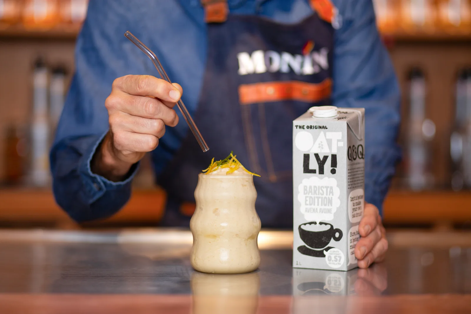 Бармен готує цитрусовий напій поруч із пакуванням Oatly Barista Edition